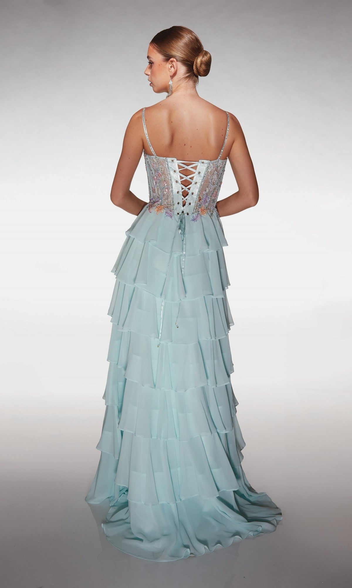 A woman faces away wearing the Alyce 61993 long prom dress, featuring a light blue pastel chiffon tiered ruffle skirt, lace-up back, and spaghetti straps, set against a plain white background.